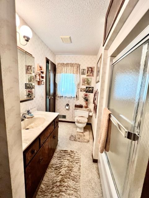 full bathroom with a textured ceiling, combined bath / shower with glass door, vanity, and toilet