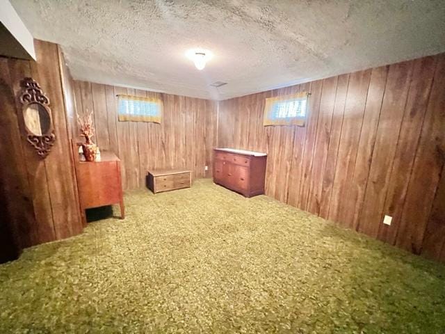 basement featuring wood walls, a textured ceiling, and carpet floors