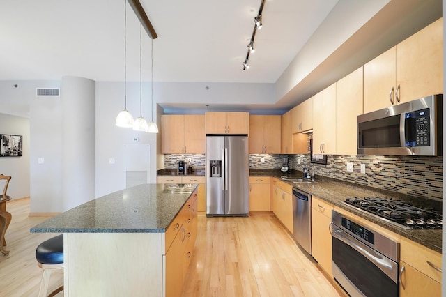 kitchen with a center island, decorative light fixtures, light brown cabinetry, appliances with stainless steel finishes, and a sink