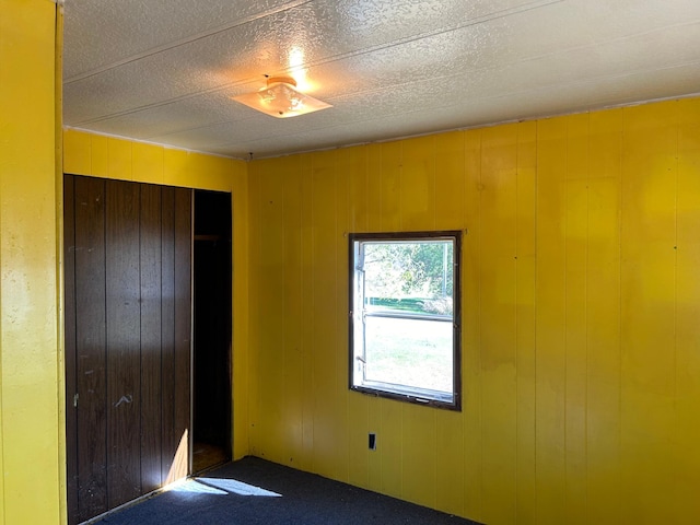 unfurnished bedroom featuring carpet floors, wooden walls, and a closet