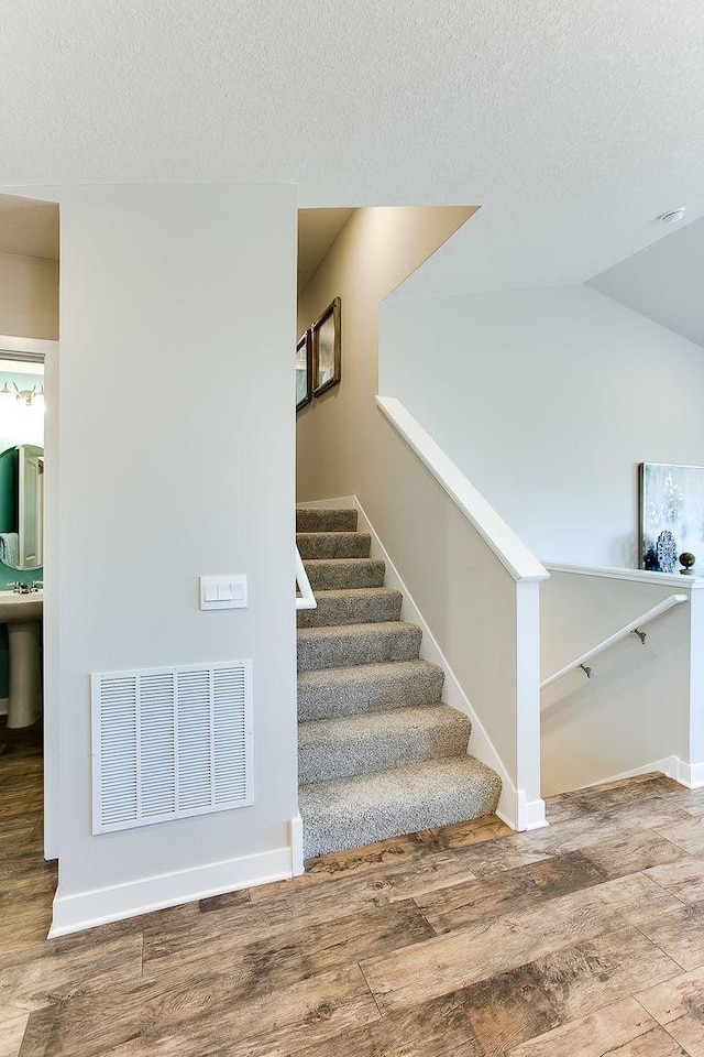 staircase with lofted ceiling, hardwood / wood-style floors, and a textured ceiling