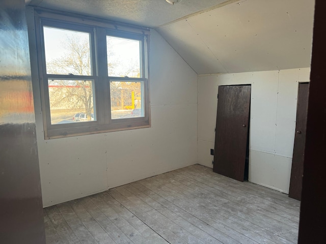 additional living space featuring vaulted ceiling, light hardwood / wood-style flooring, and a textured ceiling