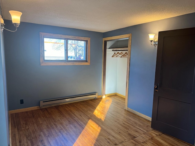 unfurnished bedroom with a textured ceiling, a baseboard heating unit, hardwood / wood-style flooring, and a closet