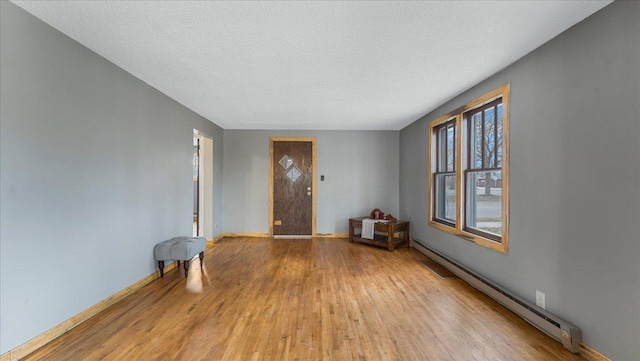 empty room with light hardwood / wood-style flooring, a baseboard heating unit, and a textured ceiling