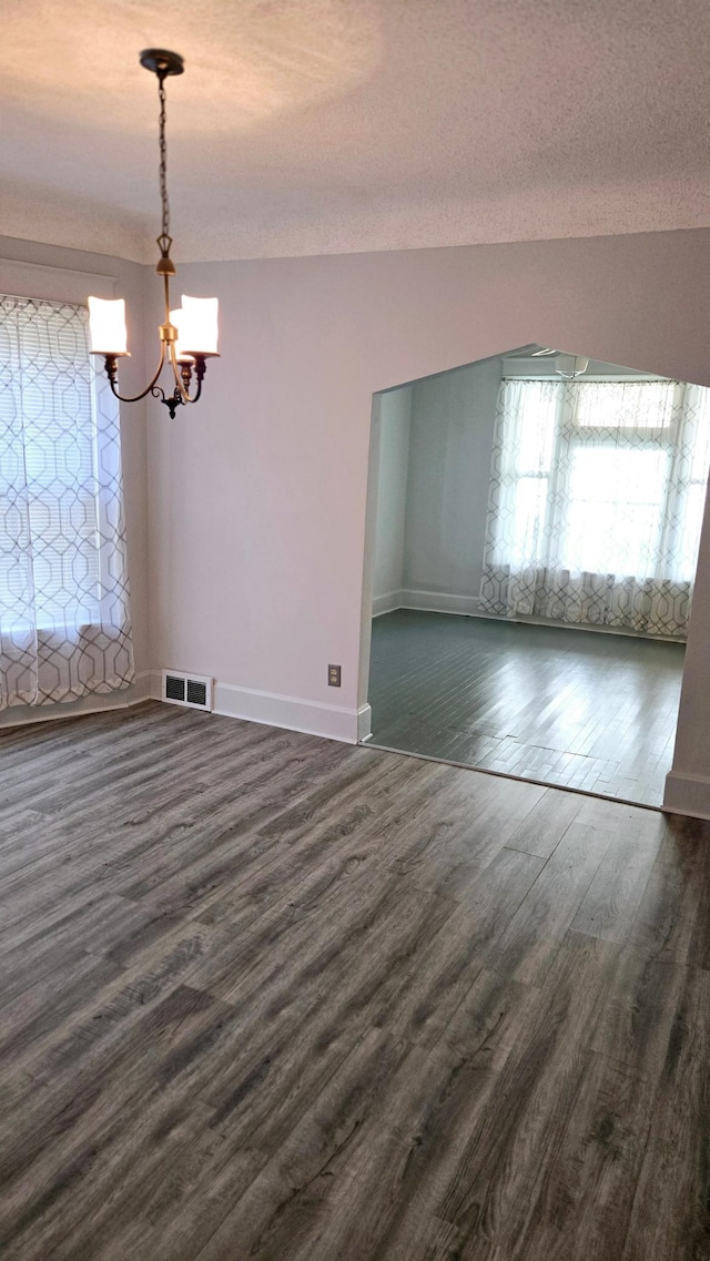 unfurnished dining area with dark hardwood / wood-style floors, a textured ceiling, and a chandelier