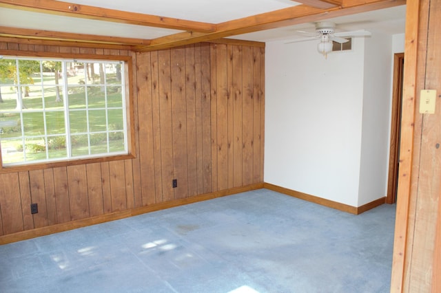 empty room with beamed ceiling, light colored carpet, wooden walls, and ceiling fan