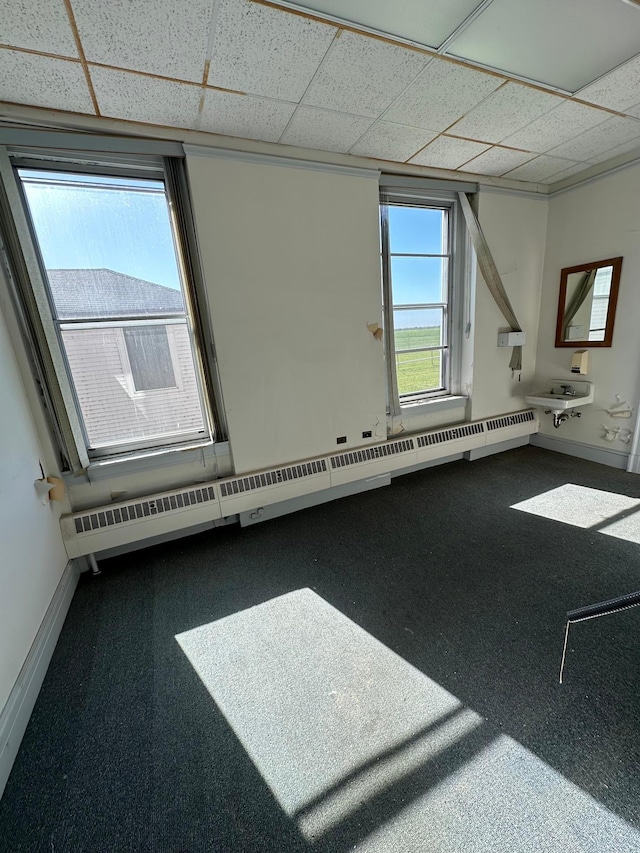 empty room featuring a baseboard radiator, carpet floors, and a paneled ceiling