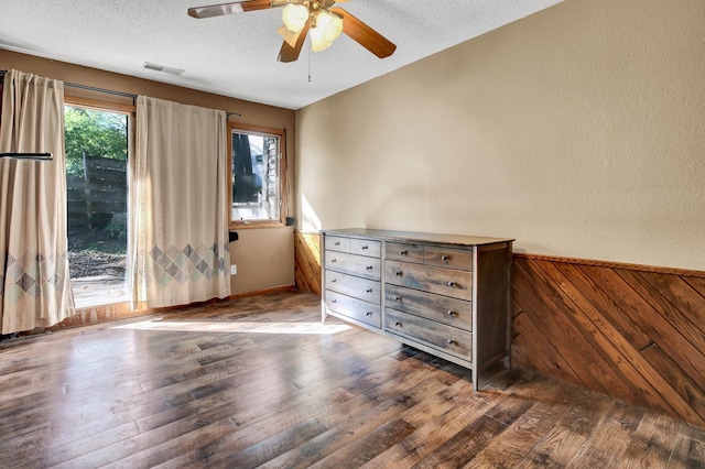 unfurnished bedroom featuring wooden walls, ceiling fan, dark hardwood / wood-style floors, and a textured ceiling