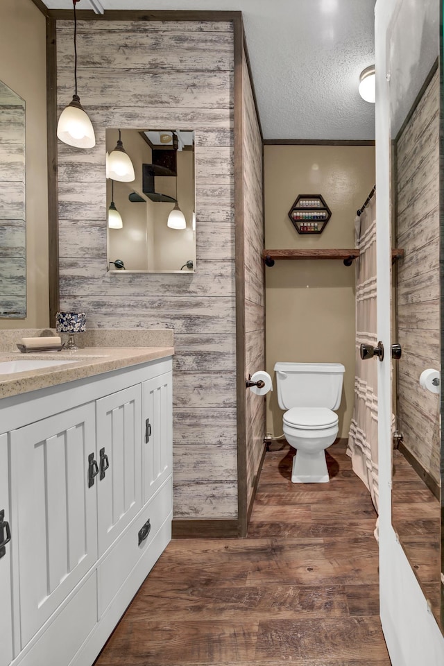 bathroom with wood walls, vanity, a textured ceiling, hardwood / wood-style flooring, and toilet