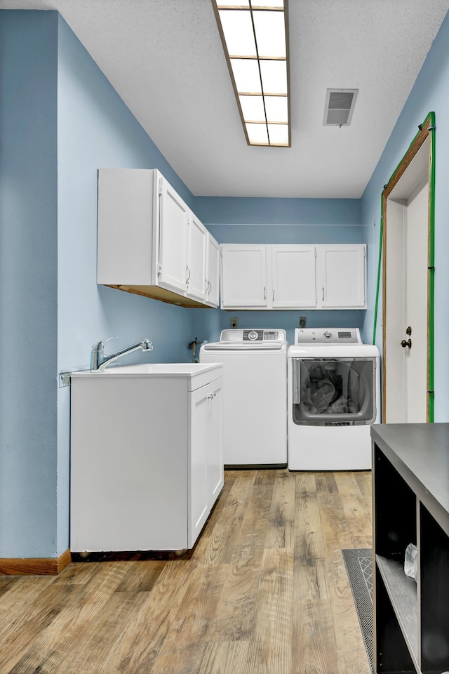 clothes washing area with a textured ceiling, light hardwood / wood-style flooring, independent washer and dryer, and cabinets