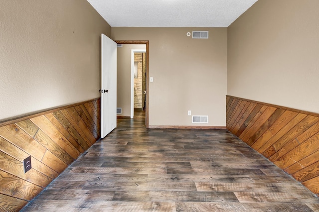 spare room featuring wood walls, a textured ceiling, and dark hardwood / wood-style floors