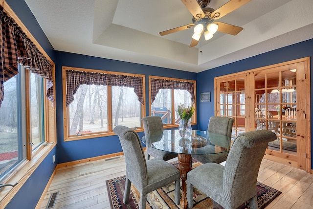 dining space featuring ceiling fan, light hardwood / wood-style flooring, french doors, and a tray ceiling