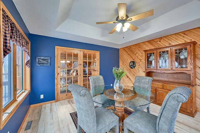 dining area featuring french doors, wooden walls, ceiling fan, and light wood-type flooring