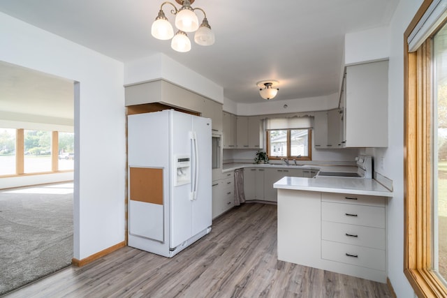 kitchen featuring stove, sink, white refrigerator with ice dispenser, a notable chandelier, and light hardwood / wood-style floors