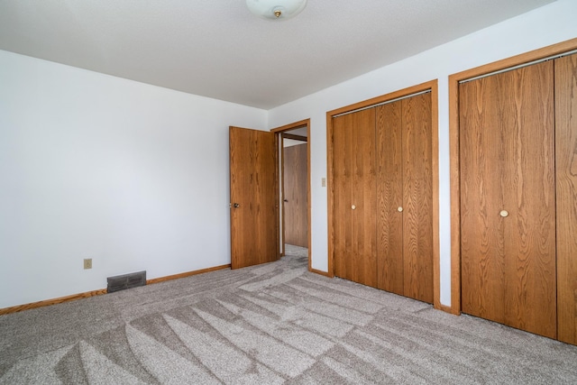 unfurnished bedroom featuring light carpet and two closets