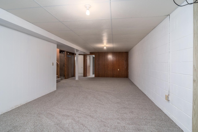 basement featuring wooden walls, carpet floors, and a paneled ceiling