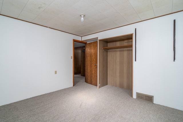 unfurnished bedroom with carpet floors, wooden walls, and a closet