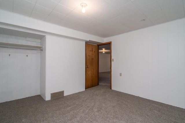 unfurnished bedroom featuring carpet floors, wood walls, and a closet