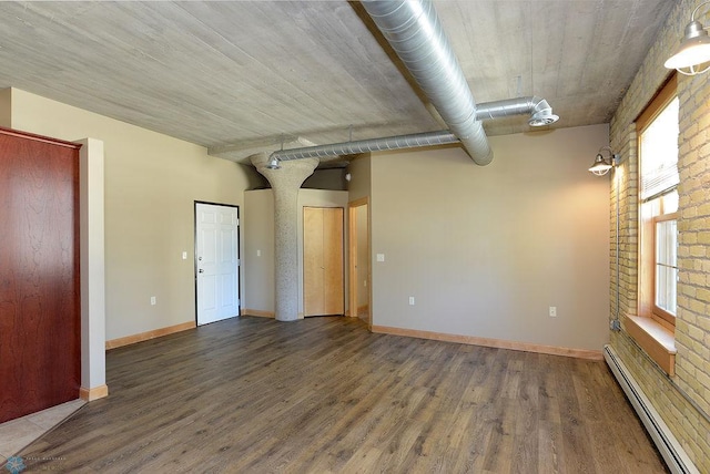 unfurnished room with brick wall, dark hardwood / wood-style floors, and a baseboard radiator