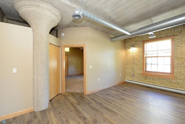 unfurnished room featuring brick wall, baseboard heating, and hardwood / wood-style floors