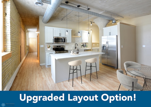 kitchen with appliances with stainless steel finishes, white cabinetry, brick wall, light wood-type flooring, and decorative light fixtures