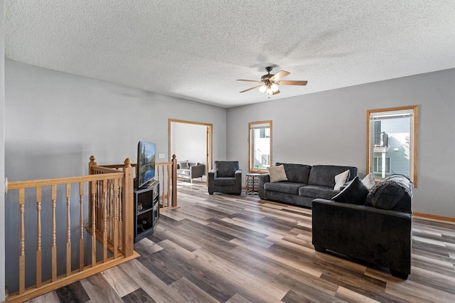 living area featuring a ceiling fan, a textured ceiling, baseboards, and wood finished floors