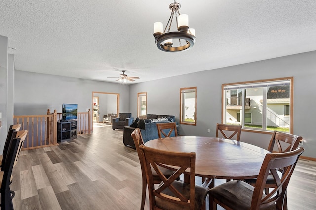 dining space featuring light wood-style flooring, a textured ceiling, and ceiling fan with notable chandelier