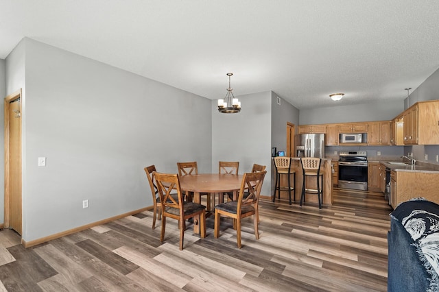 dining area featuring a textured ceiling, baseboards, a notable chandelier, and wood finished floors