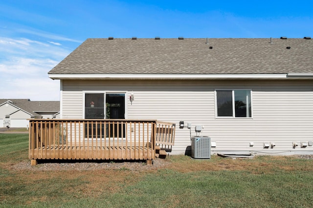 rear view of property featuring cooling unit, roof with shingles, a lawn, and a deck