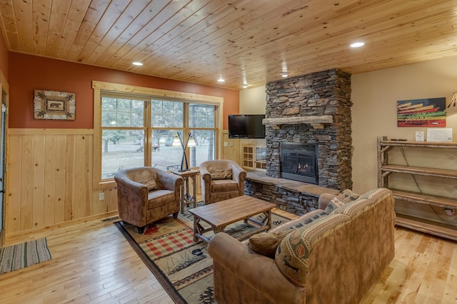 living room with light hardwood / wood-style flooring, wood ceiling, and a stone fireplace