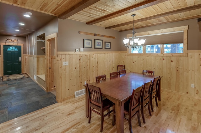 dining area featuring beam ceiling, wood ceiling, wood walls, and light hardwood / wood-style flooring