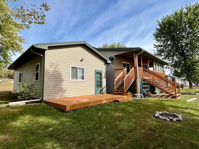 back of property with a wooden deck, a lawn, and an outdoor fire pit