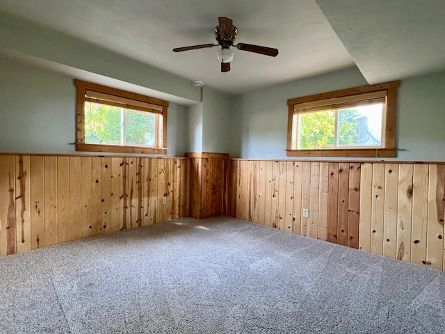 carpeted spare room with wooden walls and ceiling fan