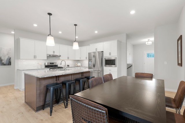 kitchen with an island with sink, appliances with stainless steel finishes, light hardwood / wood-style floors, and white cabinetry