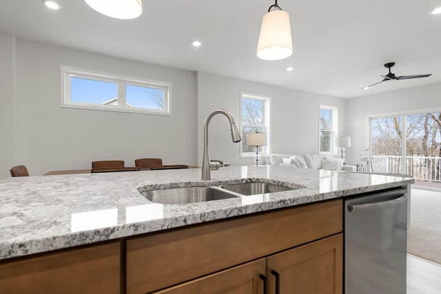 kitchen featuring light stone counters, sink, decorative light fixtures, dishwasher, and a wealth of natural light