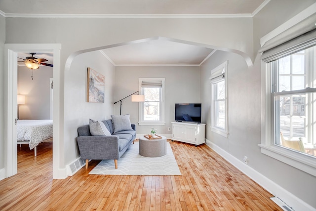 living area featuring light wood finished floors, baseboards, visible vents, and ornamental molding