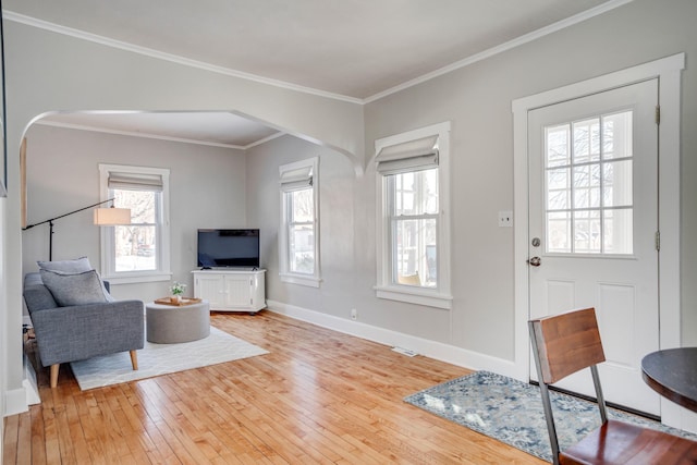 living area with wood-type flooring, baseboards, arched walkways, and ornamental molding