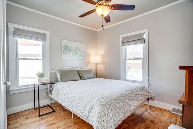 bedroom with ceiling fan, visible vents, baseboards, ornamental molding, and wood-type flooring