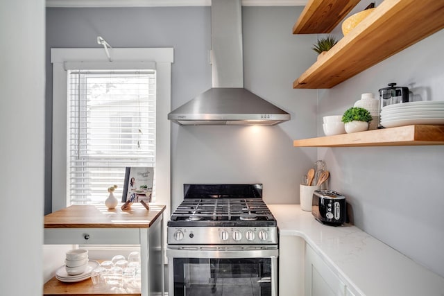 kitchen with stainless steel gas range, light countertops, wall chimney exhaust hood, and open shelves