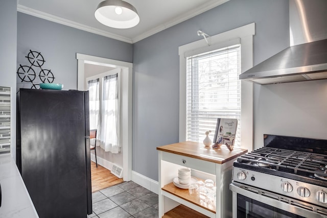 kitchen featuring visible vents, wall chimney range hood, stainless steel gas range, freestanding refrigerator, and crown molding