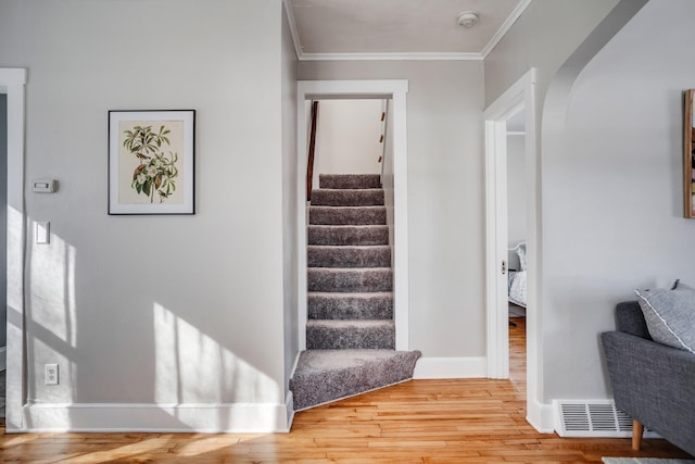 stairway featuring baseboards, visible vents, arched walkways, ornamental molding, and wood finished floors