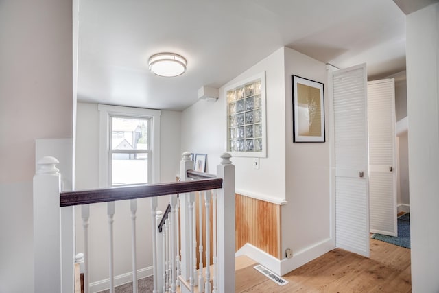 hallway with visible vents, wood finished floors, and an upstairs landing