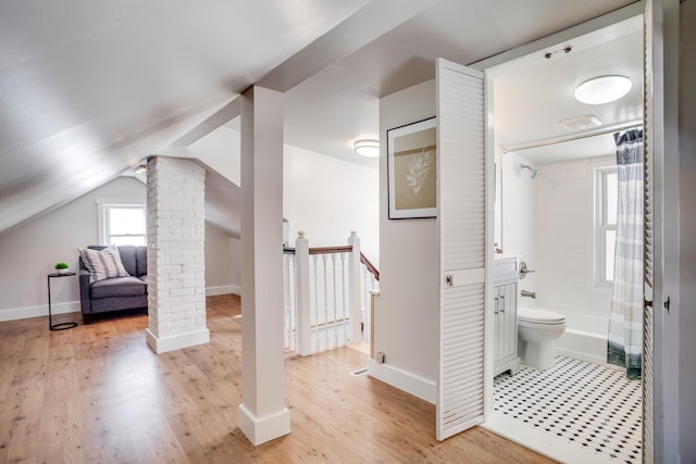 interior space featuring decorative columns, baseboards, wood finished floors, shower / bathtub combination with curtain, and vaulted ceiling