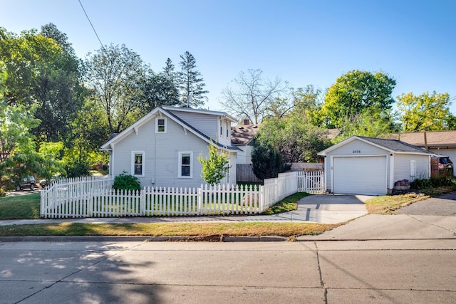 view of front of property with a fenced front yard, a detached garage, concrete driveway, and an outbuilding