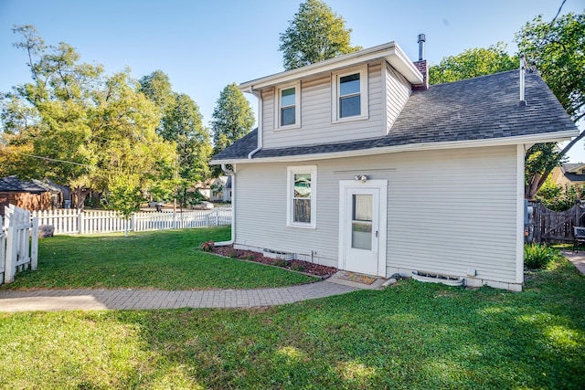 rear view of property featuring a yard, roof with shingles, and fence