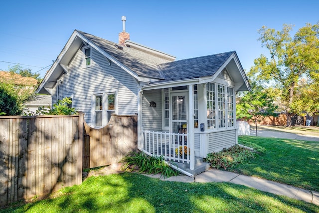 view of front of house with a shingled roof, a sunroom, a chimney, fence, and a front lawn