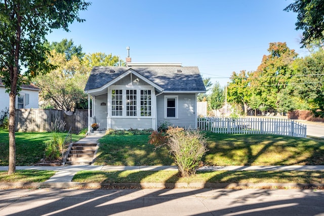 bungalow-style home with a front yard, roof with shingles, fence, and a chimney