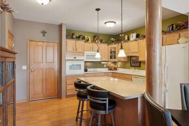 kitchen with light brown cabinets, a kitchen breakfast bar, decorative light fixtures, white appliances, and light wood-type flooring