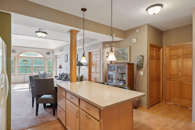 kitchen with light brown cabinetry, light wood-type flooring, hanging light fixtures, and decorative columns