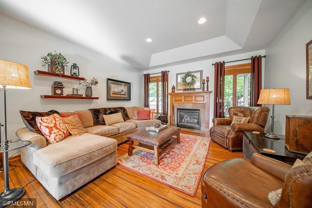 living room with a raised ceiling, light wood-type flooring, and a textured ceiling